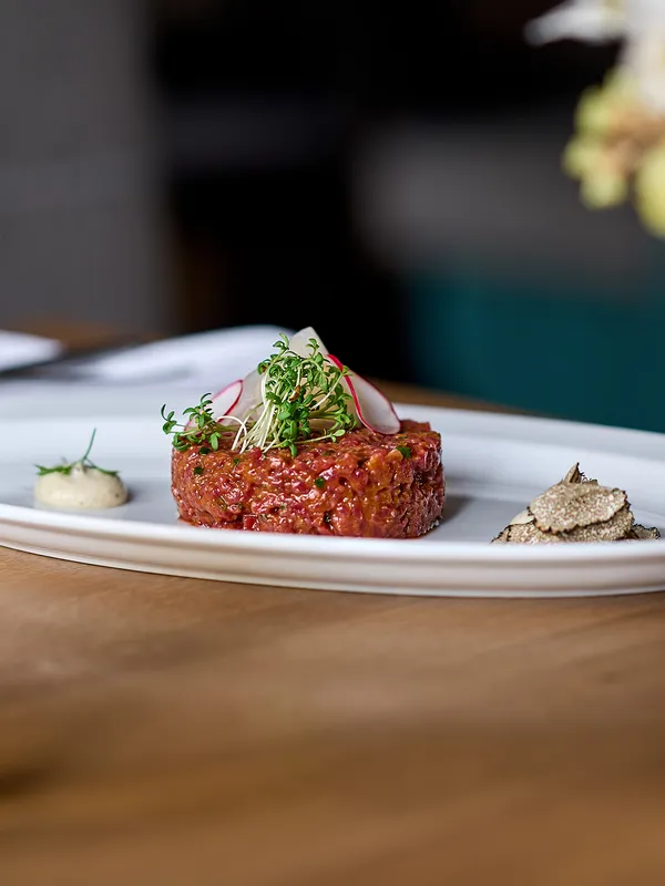 Rindertatar mit Rettich, Microgreens, Trüffel und Senfsauce auf weißem Teller mit Bier